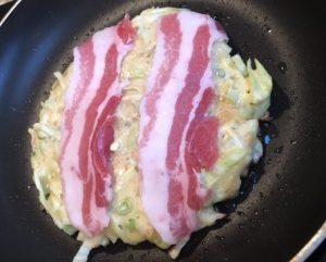Okonomiyaki with bacon ready to flip