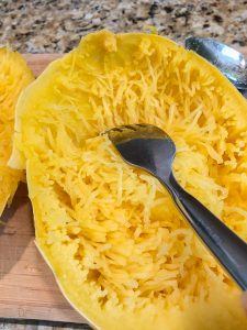 scraping meat from a cooked spaghetti squash using a fork